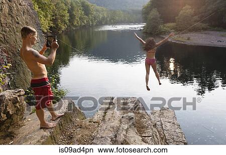 Picture - Young couple photographing jump from rock ledge, Hamburg, Pennsylvania, USA. Fotosearch