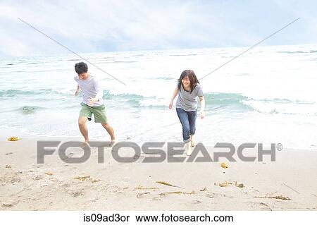 Stock Photography - Young couple running away from tide. Fotosearch