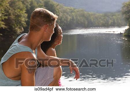 Stock Image - Young couple sitting by river, Hamburg, Pennsylvania, USA. Fotosearch