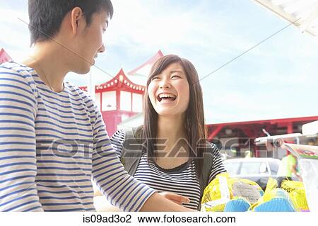 Stock Image - Young couple standing at market stall laughing. Fotosearch