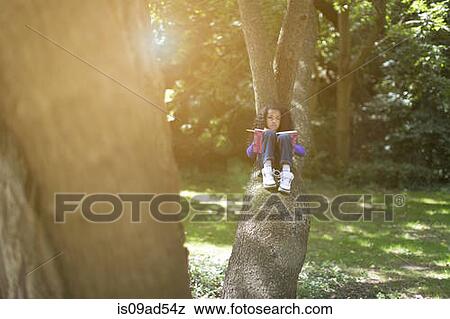 Stock Photo - Young girl lying on tree branch looking at book. Fotosearch