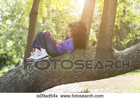 Stock Photo - Young girl lying on tree branch reading book. Fotosearch