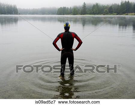 Stock Photo - Young man in wet suit preparing to swim lake. Fotosearch