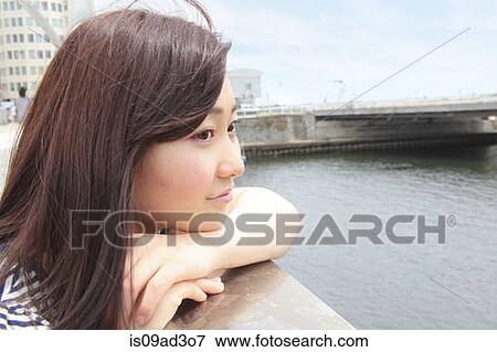 Stock Photo - Young woman leaning on railings overlooking river. Fotosearch