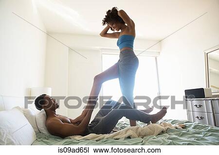 Young woman standing on bed with man lying down View Large Photo Image Stock Image - Young woman standing on bed with man lying down. Fotosearch