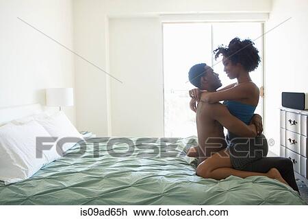 Stock Image - Young woman straddling man on bed. Fotosearch