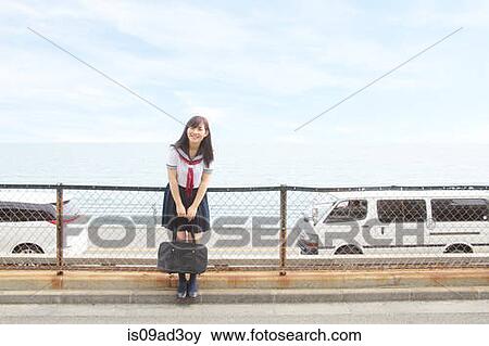 Stock Photo - Young woman wearing school uniform, carrying bag. Fotosearch