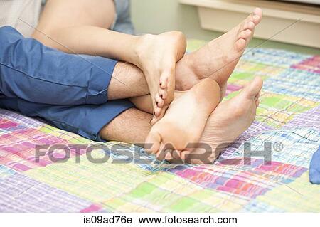 Stock Image - Close up of couples legs and feet on bed. Fotosearch