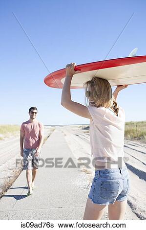 Couple carrying surfboard on coastal path, Breezy Point, Queens, New York, USA View Large Photo Image Stock Photograph - Couple carrying surfboard on coastal path, Breezy Point, Queens, New York, USA. Fotosearch