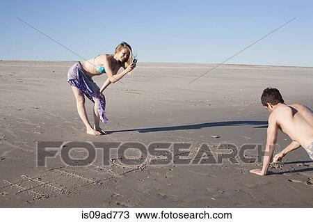 Stock Image - Couple writing message in sand, Breezy Point, Queens, New York, USA. Fotosearch
