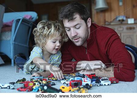 Stock Image - Father and toddler daughter playing with toy cars in sitting room. Fotosearch