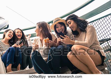Stock Photo - Five young women sitting on steps looking at smartphones. Fotosearch