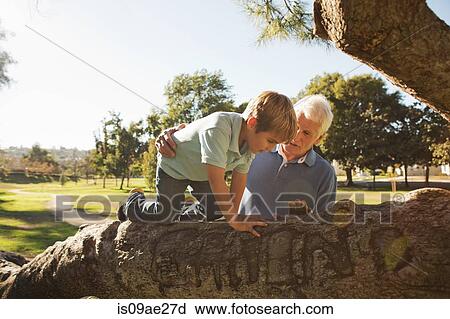 Stock Image - Grandfather helping grandson to climb tree. Fotosearch