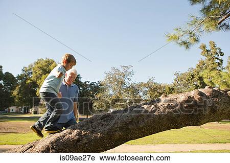 Stock Image - Grandfather helping grandson to climb tree. Fotosearch