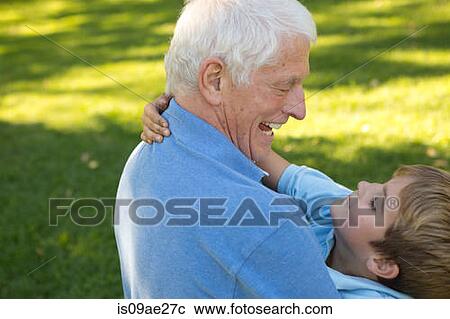 Stock Image - Grandfather kneeling on grass hugging grandson. Fotosearch
