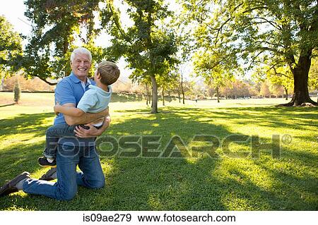 Grandfather kneeling on grass hugging grandson View Large Photo Image Stock Photo - Grandfather kneeling on grass hugging grandson. Fotosearch