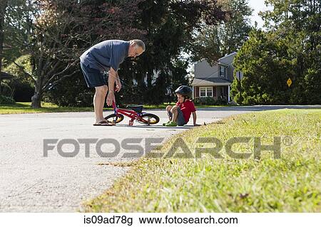 Stock Image - Grandfather picking up young boys bicycle. Fotosearch