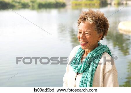 Stock Image - Portrait of senior woman by lake in park. Fotosearch