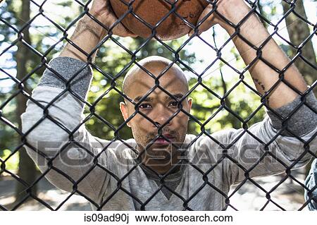 Portrait of young man holding basketball through wire fence View Large Photo Image Stock Image - Portrait of young man holding basketball through wire fence. Fotosearch