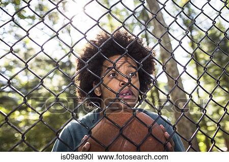 Portrait of young man holding basketball through wire fence View Large Photo Image Stock Image - Portrait of young man holding basketball through wire fence. Fotosearch