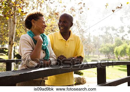 Stock Image - Senior couple leaning on footbridge in park. Fotosearch