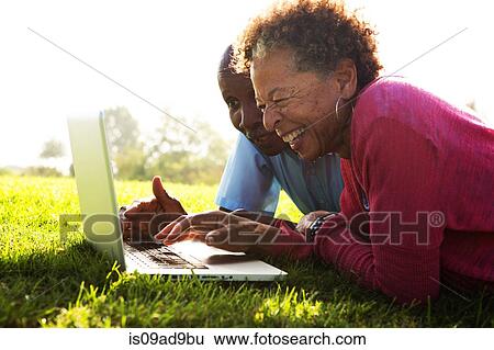 Senior couple lying in park using laptop View Large Photo Image Stock Photograph - Senior couple lying in park using laptop. Fotosearch
