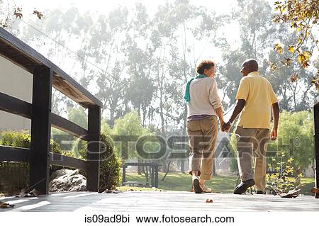 Senior couple walking on footbridge in park View Large Photo Image Stock Image - Senior couple walking on footbridge in park. Fotosearch