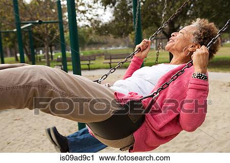 Stock Image - Senior woman on swing in park. Fotosearch
