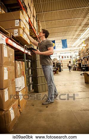 Stock Image - Worker in warehouse selecting items from cardboard boxes. Fotosearch