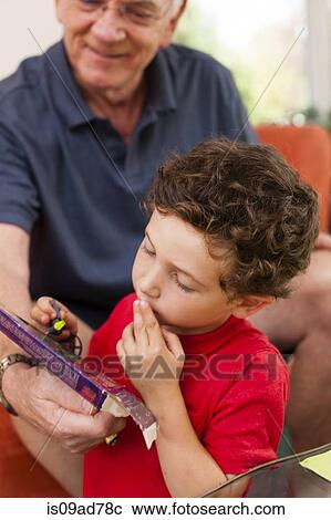 Stock Image - Young boy and grandfather playing game in sitting room. Fotosearch