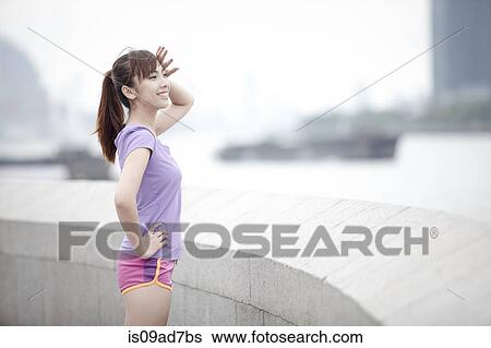 Young female jogger standing by wall View Large Photo Image Stock Photograph - Young female jogger standing by wall. Fotosearch