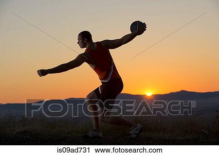 Stock Image - Young man preparing to throw discus at sunset. Fotosearch