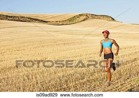 Stock Photo - Young woman running across field, Bainbridge Island, Washington State, USA. Fotosearch