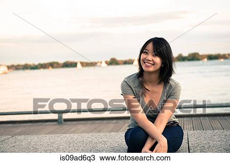 Young woman sitting at waterfront View Large Photo Image Stock Image - Young woman sitting at waterfront. Fotosearch