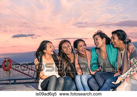 Young women lying sitting at waterfront at dusk with arms around View Large Photo Image Stock Photography - Young women lying sitting at waterfront at dusk with arms around. Fotosearch