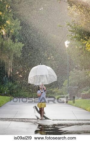 Barefoot girl holding up umbrella and walking through puddles on street View Large Photo Image Stock Photo - Barefoot girl holding up umbrella and walking through puddles on street. Fotosearch