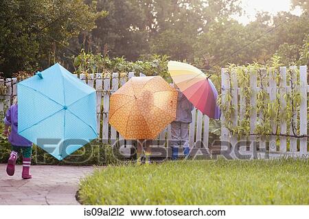 Stock Image - Boy and two sisters playing in garden carrying umbrellas. Fotosearch