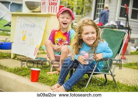 Stock Photo - Candid portrait of two smiling girls selling lemonade and popcorn at yard sale. Fotosearch
