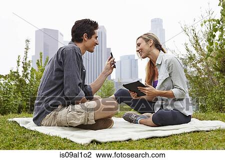 Stock Image - Couple relaxing in park by city. Fotosearch
