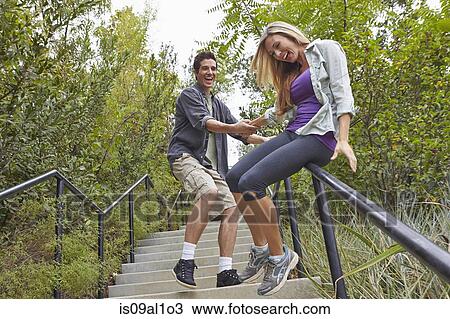 Stock Image - Couple sliding down step railing in forest. Fotosearch