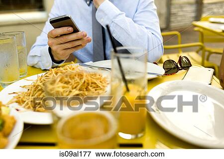 Stock Photo - Cropped shot of young man texting on smartphone at sidewalk cafe. Fotosearch