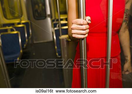 Stock Photograph - Cropped shot of young woman wearing red dress on subway train. Fotosearch