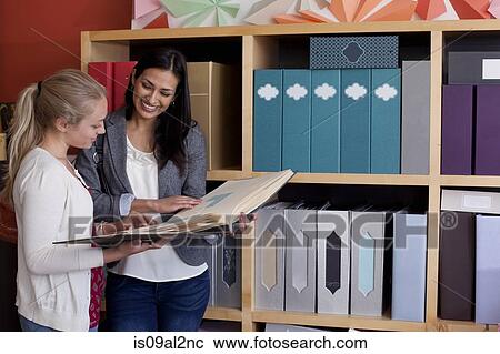 Stock Image - Customer and sales assistant browsing samples in stationery shop. Fotosearch