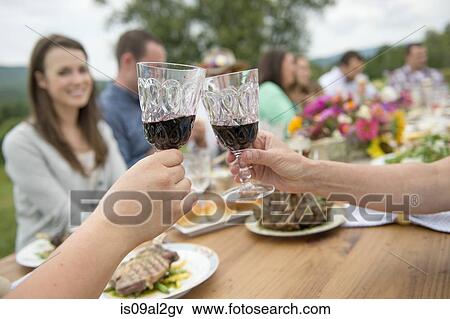 Stock Photo - Family and friends making a toast at outdoor meal. Fotosearch