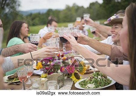 Stock Photo - Family and friends making a toast at outdoor meal. Fotosearch