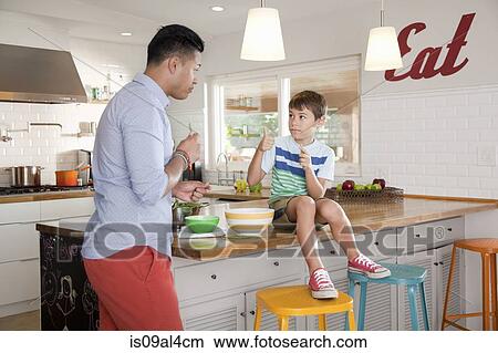Picture - Father and son in kitchen, boy sitting on counter. Fotosearch