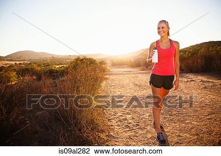 Stock Image - Female jogger holding water bottle on path, Poway, CA, USA. Fotosearch