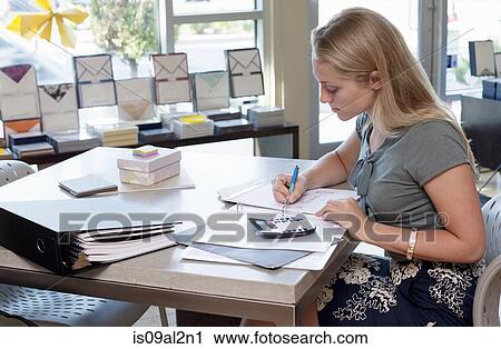 Stock Image - Female sales assistant doing paperwork in stationery shop. Fotosearch