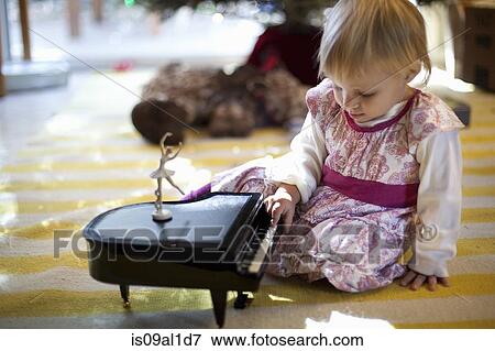 Stock Photo - Female toddler sitting on living room floor playing with toy piano music box at Xmas. Fotosearch