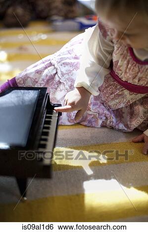 Stock Photograph - Female toddler sitting on living room floor playing toy piano music box at Xmas. Fotosearch